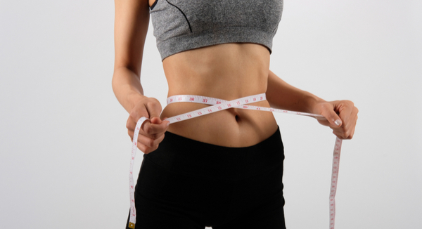 Young woman in active wear measures stomach with measuring tape.