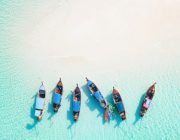 six long-tail boats wait on sandbar in aqua Phuket waters