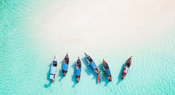 six long-tail boats wait on sandbar in aqua Phuket waters