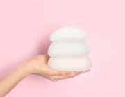 woman holds 3 sizes of breast implants against pink background.