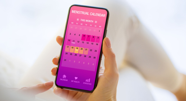 Woman holds digital menstrual calendar on mobile phone ahead of plastic surgery procedure.